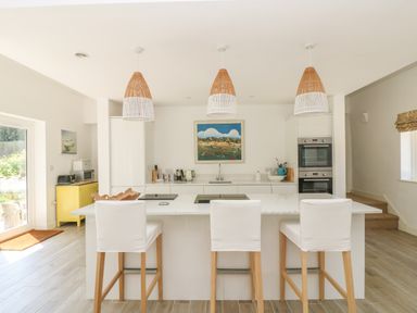 A kitchen with a white island and three chairs under hanging lights at Little Chycoose in Truro