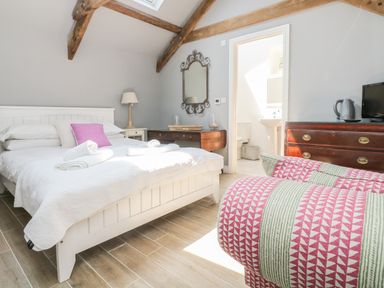 A bedroom with a white bed and folded towels a wooden dresser with a kettle a wall mirror and a doorway leading to a bathroom at Little Chycoose in Truro