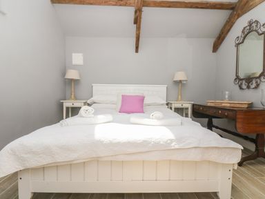 A bedroom with a white bed with pink pillow two bedside tables with lamps and a wooden dresser with mirror at Little Chycoose in Truro