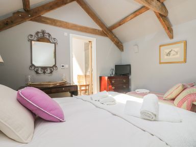A bedroom with wooden beams a bed with white linens and rolled towels a dresser with a tv and a desk with a mirror at Little Chycoose in Truro