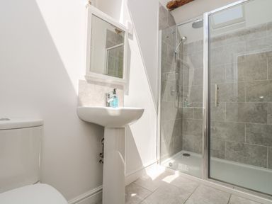A bathroom with a toilet pedestal sink mirror and a glass shower enclosure with tiled walls at Little Chycoose in Truro