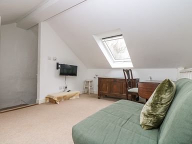 An attic room with a green sofa a wooden chair a desk an antique wooden cabinet a small wall-mounted TV and a skylight window at Little Chycoose in Truro