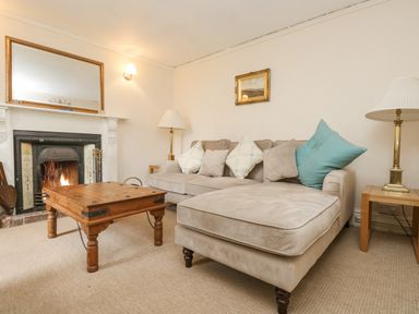 A living room with a beige sectional sofa a wooden coffee table and a fireplace at Little Chycoose in Truro
