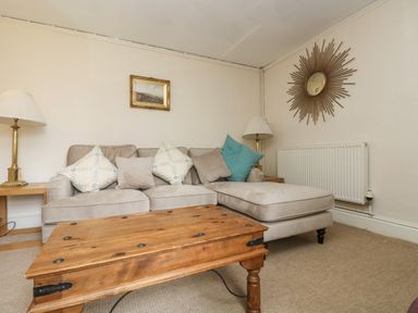 A living room with a beige sofa cushions wooden coffee table lamps and a decorative mirror at Little Chycoose in Truro