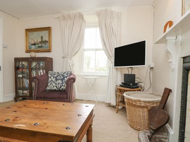 A living room with an armchair next to a bookcase and a wall mounted TV at Little Chycoose in Truro