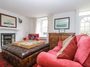 A living room with red sofas a brown leather ottoman and wooden cabinet with framed pictures at Little Chycoose in Truro