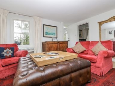 A living room with red armchairs a brown leather ottoman a wooden sideboard and a large mirror at Little Chycoose in Truro