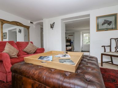 A living room with a red sofa a large wooden tray on a brown leather ottoman and framed horse artwork at Little Chycoose in Truro