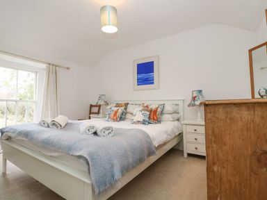A bedroom with a white bed with boat-themed pillows beside white bedside tables with lamps and a wooden dresser at Little Chycoose in Truro
