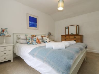 A bedroom with a double bed pillows bedside tables lamps a wooden dresser with a mirror and a blue painting on the wall at Little Chycoose in Truro