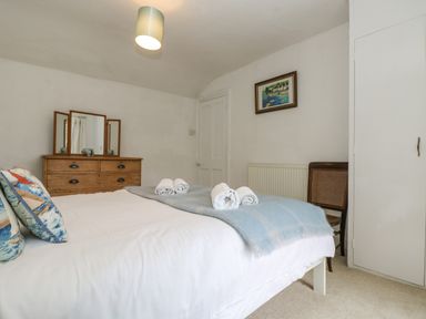 A bedroom with a bed with patterned pillows and rolled towels a wooden dresser with a mirror a chair and a framed painting on the wall at Little Chycoose in Truro