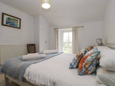 A bedroom with a bed with patterned pillows and a window with curtains at Little Chycoose in Truro