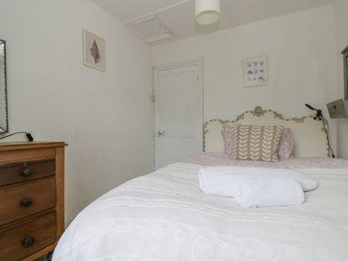 A bedroom with a bed with pillows and folded towels a wooden dresser and framed pictures on the wall at Little Chycoose in Truro