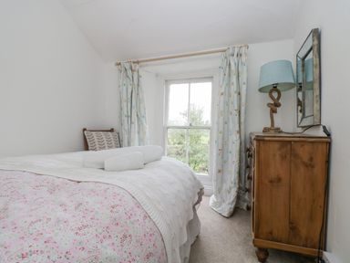 A small bedroom with a bed, wooden chest of drawers with a lamp and mirror near window at Little Chycoose in Truro