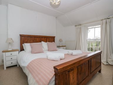 A bedroom with a wooden bed framed by two bedside tables with lamps and a window with curtains at Little Chycoose in Truro
