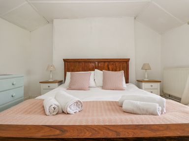 A bedroom with a wooden bed frame two striped pillows rolled white towels on the bed two bedside tables with lamps and a light blue chest of drawers at Little Chycoose in Truro