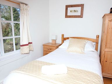 A bedroom with a single bed next to a window and wooden furniture at Rose Cottage in Manaccan