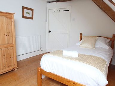 A bedroom with a single bed wooden wardrobe framed picture on wall and a white door at Rose Cottage in Manaccan