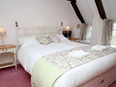 A bedroom with a large bed two bedside tables lamps floral cushions and curtains at Rose Cottage in Manaccan