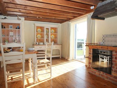 A kitchen with wooden floor and ceiling beams a dining table with chairs and a brick oven at Rose Cottage in Manaccan