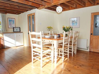 A dining room with a wooden table and six chairs with flowers and tableware at Rose Cottage in Manaccan