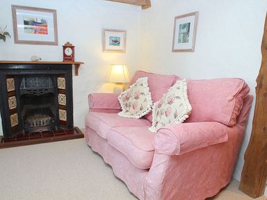 A living room with a pink sofa near a fireplace and a lamp at Rose Cottage Manaccan