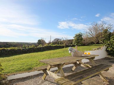 An outdoor picnic table with a basket and glasses of orange juice on grass and gravel at Rose Cottage in Manaccan