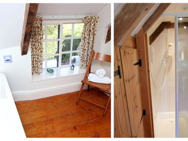 A room with wooden floor a chair with towels next to a window with floral curtains and a wooden door leading to a shower at Rose Cottage in Manaccan