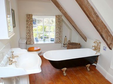 A bathroom with a clawfoot bathtub a sink a toilet and a window with floral curtains at Rose Cottage in Manaccan