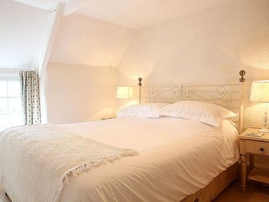 A bedroom with a large bed and two bedside tables with lamps at Rose Cottage in Manaccan