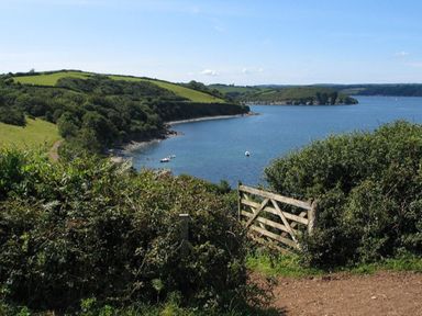 A coastal landscape with green hills and a wooden gate by the water at Rose Cottage in Manaccan