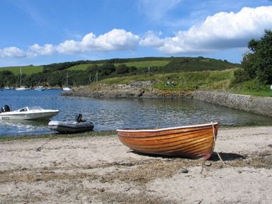 A sandy shore with boats near a body of water and grassy hills in the background at Rose Cottage in Manaccan