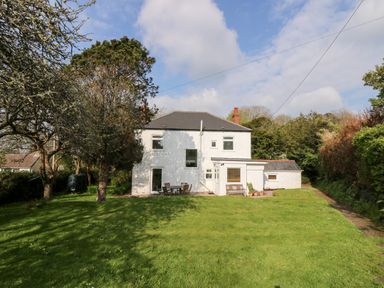 A white two-story house with a gray roof surrounded by trees and a grass lawn with outdoor furniture at Banneth in Helford