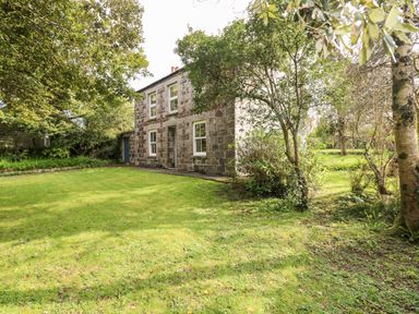 A stone house with four windows and a door surrounded by trees and grass at Banneth in Helford
