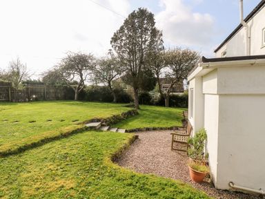 A garden with grass, trees, a gravel seating area, and a white building at Banneth in Helford