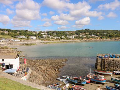 A coastal scene with boats docked near a rocky shore and houses on a hillside at Banneth in Helford