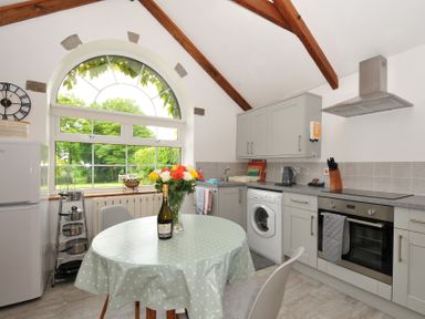 A kitchen with a table and chairs beside a window at Trevenning Chapel near Port Isaac