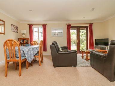 A living room with a dining table set and leather sofas facing a television at Cuckoo's Cottage in Falmouth
