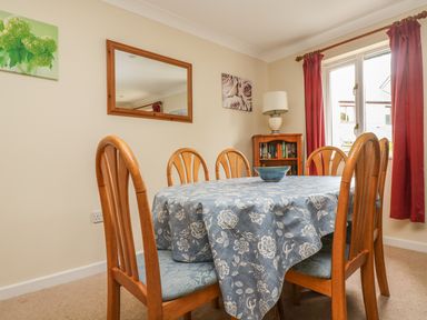 A dining room with a wooden table covered by a floral tablecloth and six wooden chairs at Cuckoo's Cottage in Falmouth