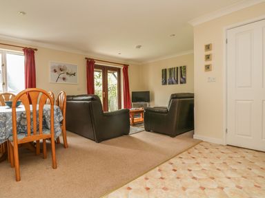 A living room with two black armchairs a wooden coffee table a dining table with chairs and red curtains at Cuckoo's Cottage in Falmouth