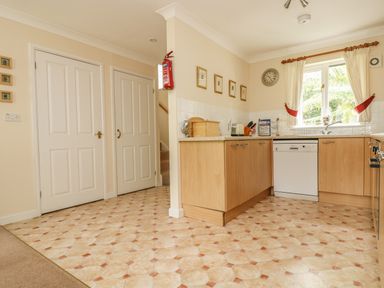 A kitchen with wooden cabinets a dishwasher a window with curtains and a tiled floor at Cuckoo's Cottage in Falmouth