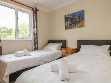 A bedroom with two single beds white bedding a wooden nightstand and a window with floral curtains at Cuckoos Cottage in Falmouth