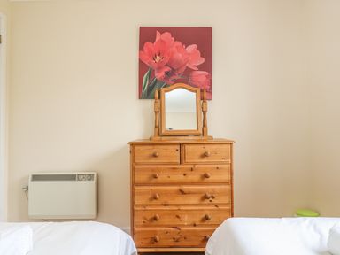 A wooden dresser with a mirror and a flower painting above it between two beds in a bedroom at Cuckoo's Cottage in Falmouth