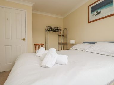 A bedroom with a made bed and rolled towels on it a chair a metal shelving unit a bedside lamp and a framed picture on the wall at Cuckoo's Cottage in Falmouth