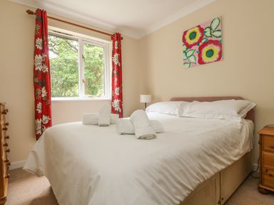 A bedroom with a bed with white linens and rolled towels a window with red floral curtains and wooden furniture at Cuckoo's Cottage in Falmouth