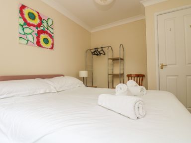 A bedroom with a double bed white towels on the bed a chair a clothes rack with hangers and a colorful flower painting on the wall at Cuckoo's Cottage in Falmouth