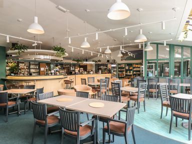 A dining area with tables, chairs, pendant lights, bar counter, and shelves with products at Cuckoo's Cottage in Falmouth