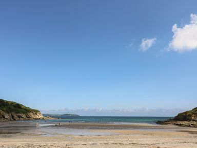 A sandy beach with shallow water and rocky cliffs on both sides at Cuckoo's Cottage in Falmouth