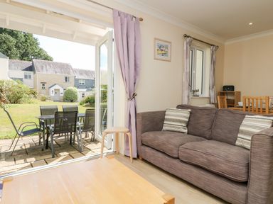 A living room with a brown sofa and striped cushions next to open glass doors leading to a patio with a black table and chairs at Trelease in Falmouth