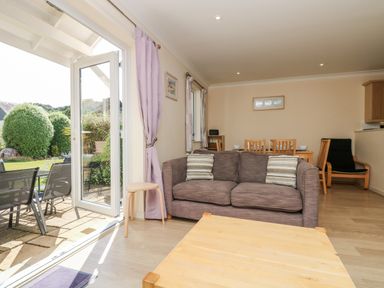 A living room with a brown sofa and wooden coffee table next to an open glass door leading to a garden at Trealse in Falmouth